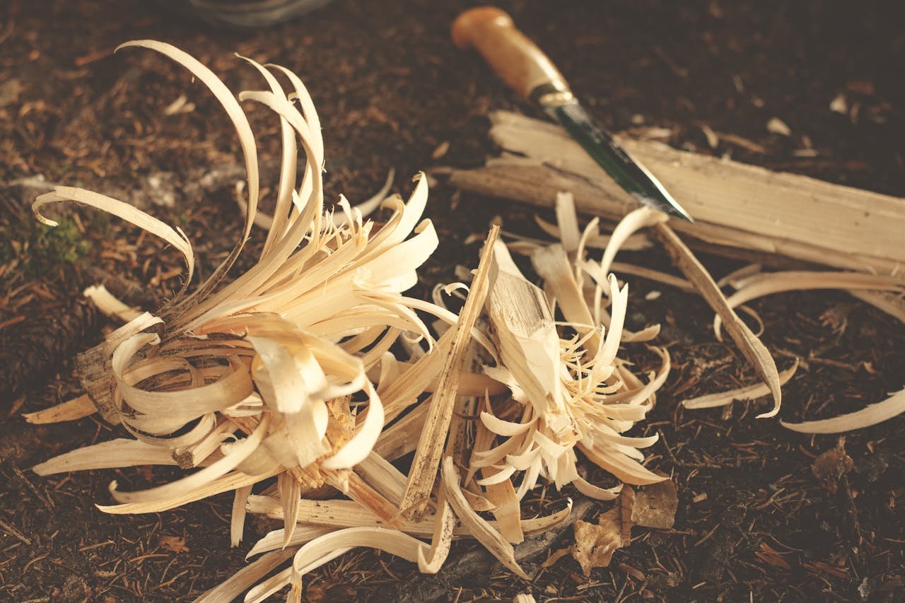 Home Woodworking knife and wood shavings on ground, showcasing craftsmanship in a rustic outdoor environment.